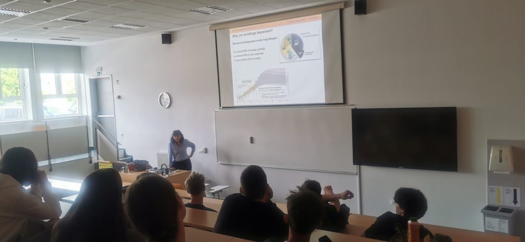 Predavalnica s skupino dijakov, ki sedijo in poslušajo predavateljico prof. dr. Živa Kristl ob projekciji z naslovom 'Why are U.S. equity markets important?'. Na projekciji so prikazani grafi in tortni diagrami. Predavateljica stoji ob mizi z računalnikom.