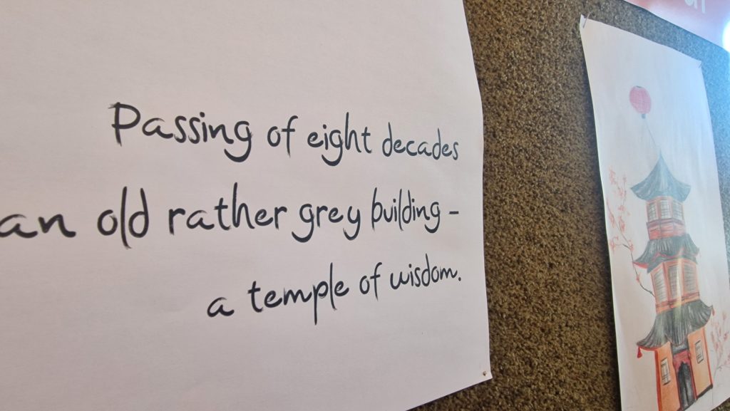 List papirja z napisanim haikujem v angleščini: ‘Passing of eight decades / an old rather grey building – / a temple of wisdom.’ Ob njem je razstavljena risba pagode v japonskem ali kitajskem slogu, narisana s svinčnikom in barvicami na belem papirju