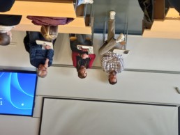 Trije gostje sedijo v učilnici za mizami, pred njimi so odprti zvezki. Na levi sedi Zlatko Stojiljković (bil je sin izbrisanih staršev), na sredini Katarina Keček (bila je med izbrisanimi), na desni Irfan Beširović (bil je med izbrisanimi). V ozadju so lesene mize in stolčki, na levi strani slike je viden del projekcijskega zaslona z modrim ozadjem.